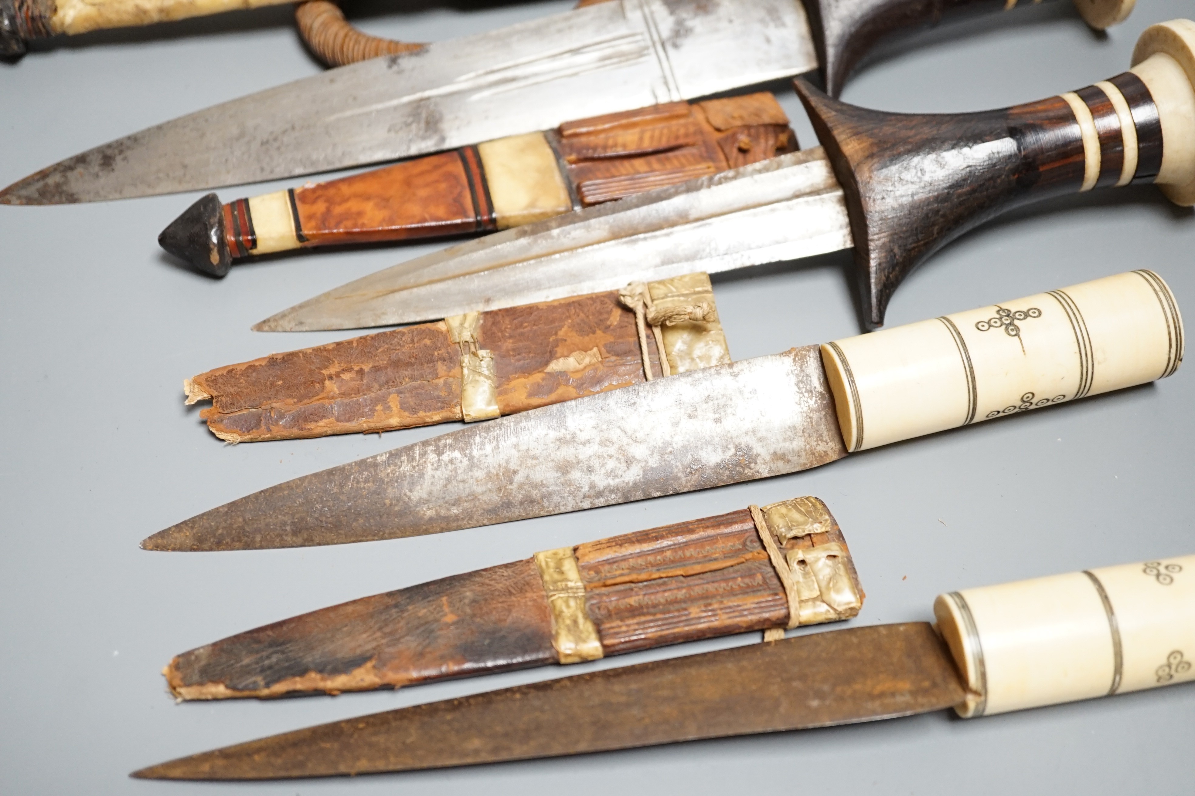 Five assorted African Nilotic tribal daggers c.1900, comprising three with turned ivory mounted ebony handles (two with silver pommels); and two further with cylindrical ivory handles, all in their leather sheaths, maxim